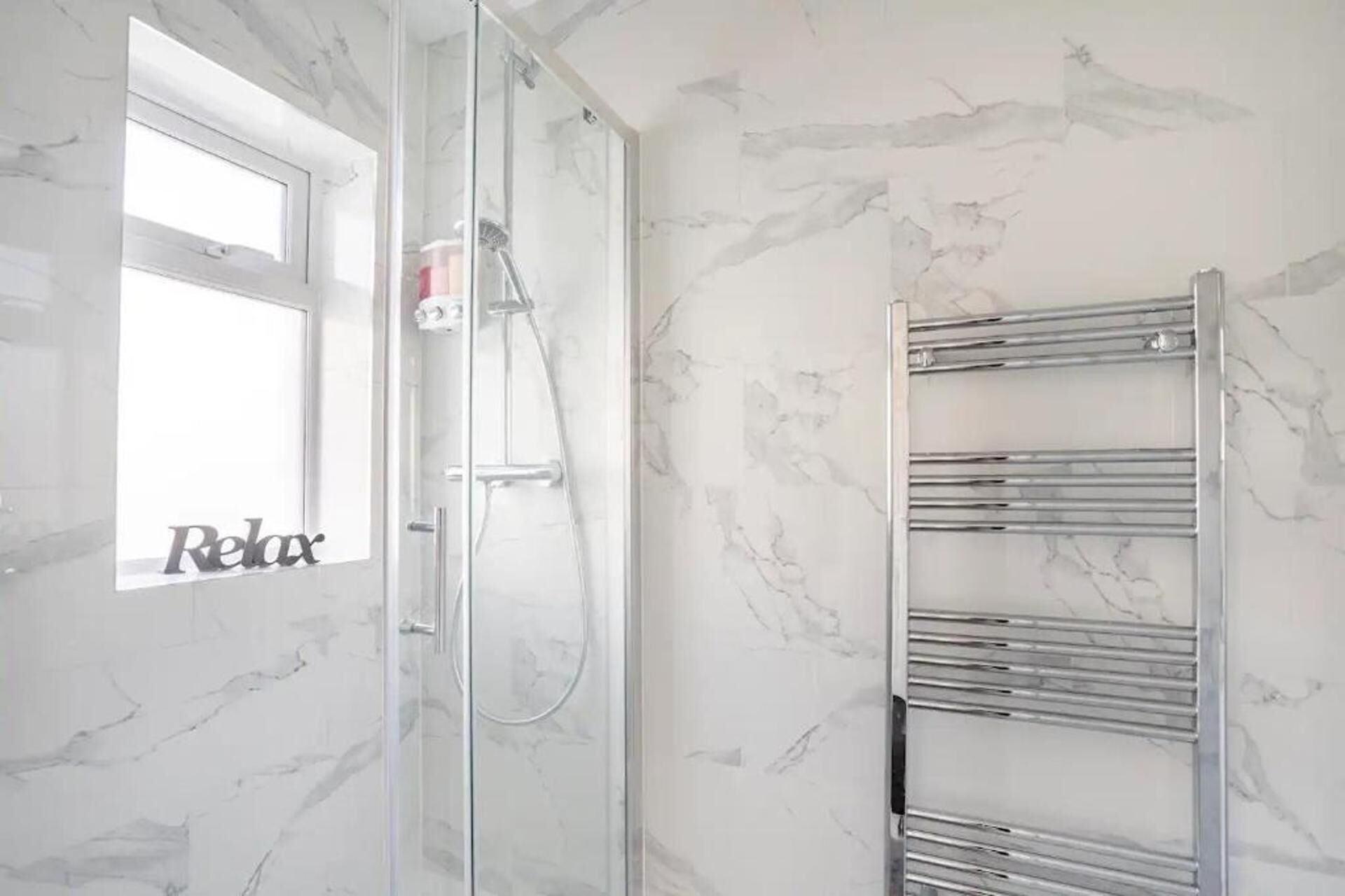 A bathroom with a glass shower enclosure, a towel rack, and a marble wall.