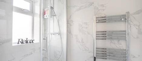 A bathroom with a glass shower enclosure, a towel rack, and a marble wall.