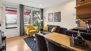 A modern living room with a sofa, a yellow armchair, a dining table, and a kitchen area with a sink and countertop. - Charysma: Aurum Suite | modern & elegant design | parking lot | terrace (Hameln)