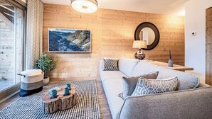 Een moderne woonkamer met een houten wand, een groot raam, een bank, een salontafel en een schilderij van een berglandschap.