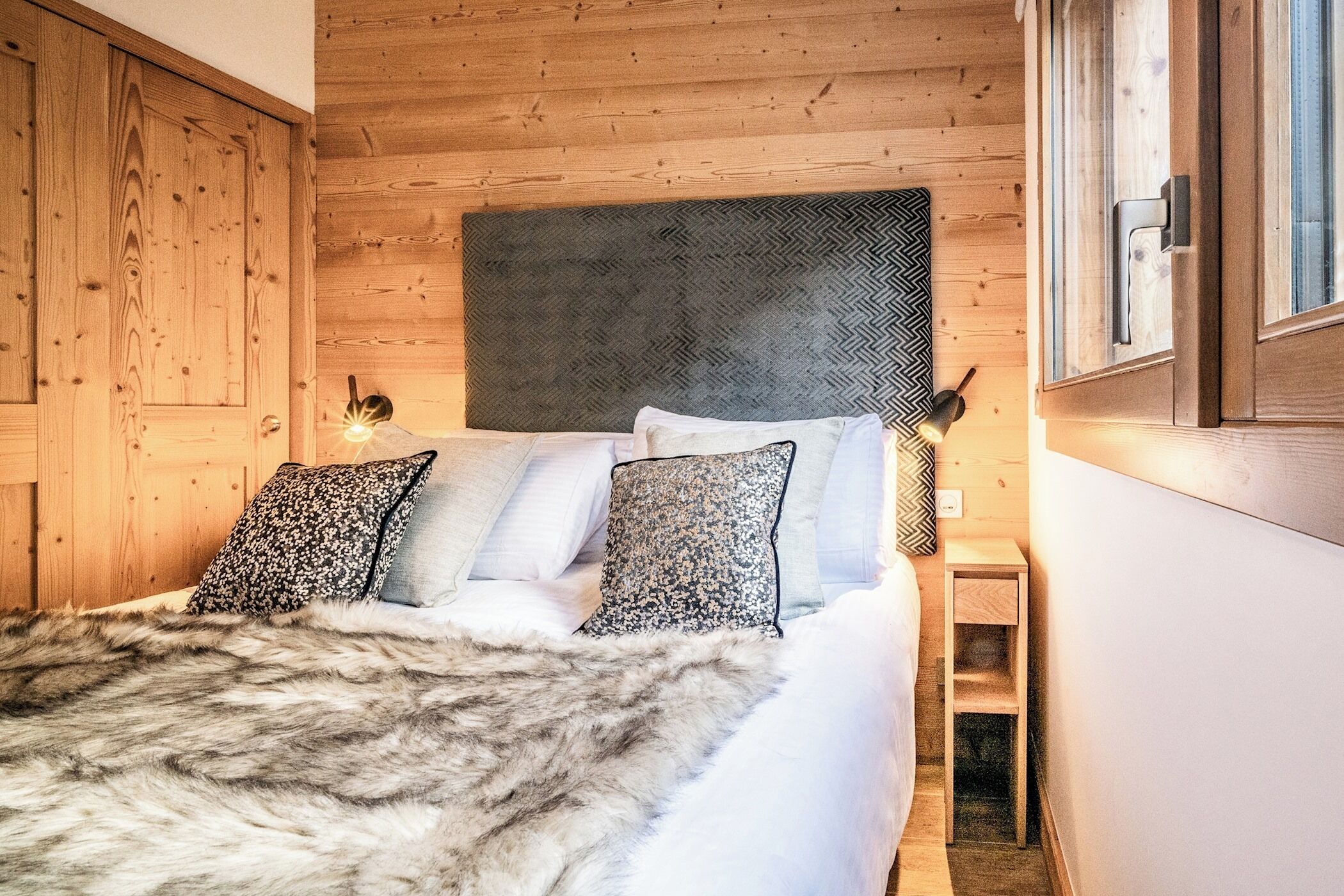Ein Schlafzimmer mit Holzwänden, einem Bett, Kissen und einem Nachttisch.