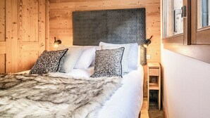 Een slaapkamer met houten lambrisering, een bed, kussens en een nachtkastje.