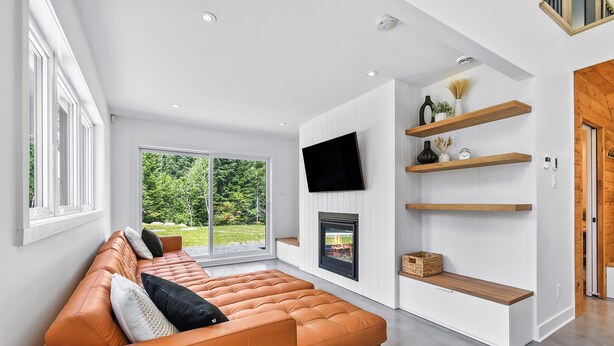 Een moderne woonkamer met een leren bank, een open haard, ingebouwde planken en een aan de muur bevestigde televisie.