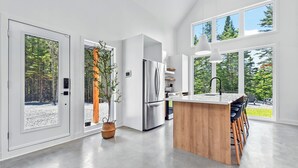 Een moderne keuken met grote ramen, een roestvrijstalen koelkast en een houten kookeiland met barstoelen.