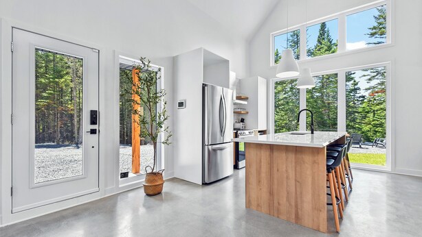 Een moderne keuken met grote ramen, een roestvrijstalen koelkast en een houten kookeiland met barstoelen.