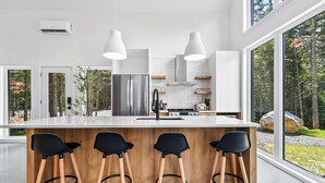 Een moderne keuken met een groot kookeiland, barstoelen en uitzicht op het bos.
