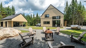 Een moderne lodge met een grote stenen openhaard, zitplaatsen buiten en uitzicht op het omliggende bos.