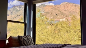 Ein Schlafzimmer mit einem großen Fenster, das einen Blick auf eine gebirgige Landschaft und ein Gebäude bietet.