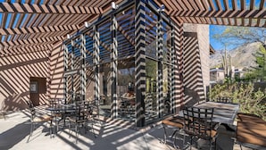 Eine Terrasse im Freien mit einer geometrischen Metall-Dachkonstruktion, umgeben von Tischen und Stühlen.