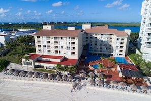 A hotel with multiple floors, a swimming pool, and a beach area with umbrellas.