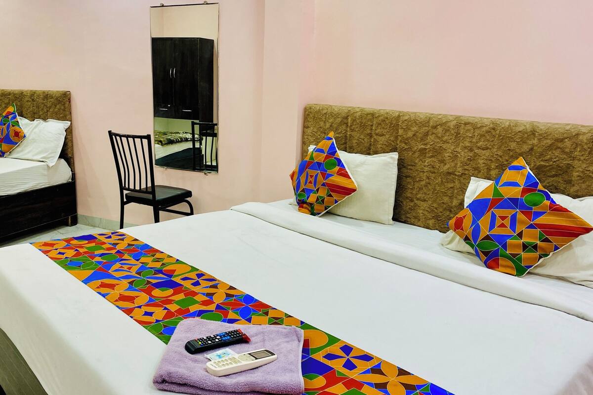 A hotel room with two beds, a chair, a mirror, and a colorful geometric-patterned bedspread.