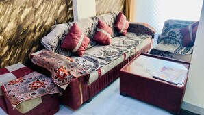 A sofa with patterned cushions, a matching throw blanket, and a small table with a newspaper. - Hotel Dev Shree (Indore)