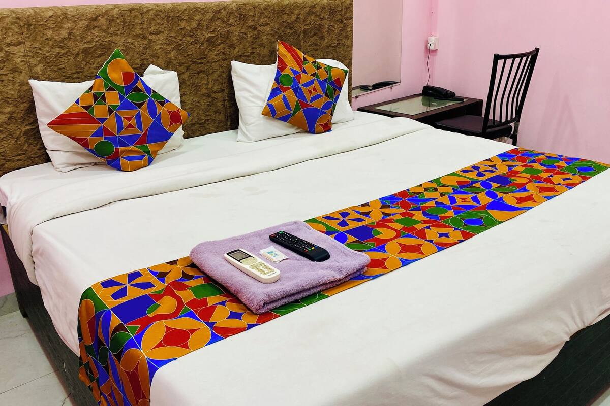 A neatly made bed with a colorful geometric-patterned bedspread and pillows, a remote control, and a mobile phone on a purple towel.