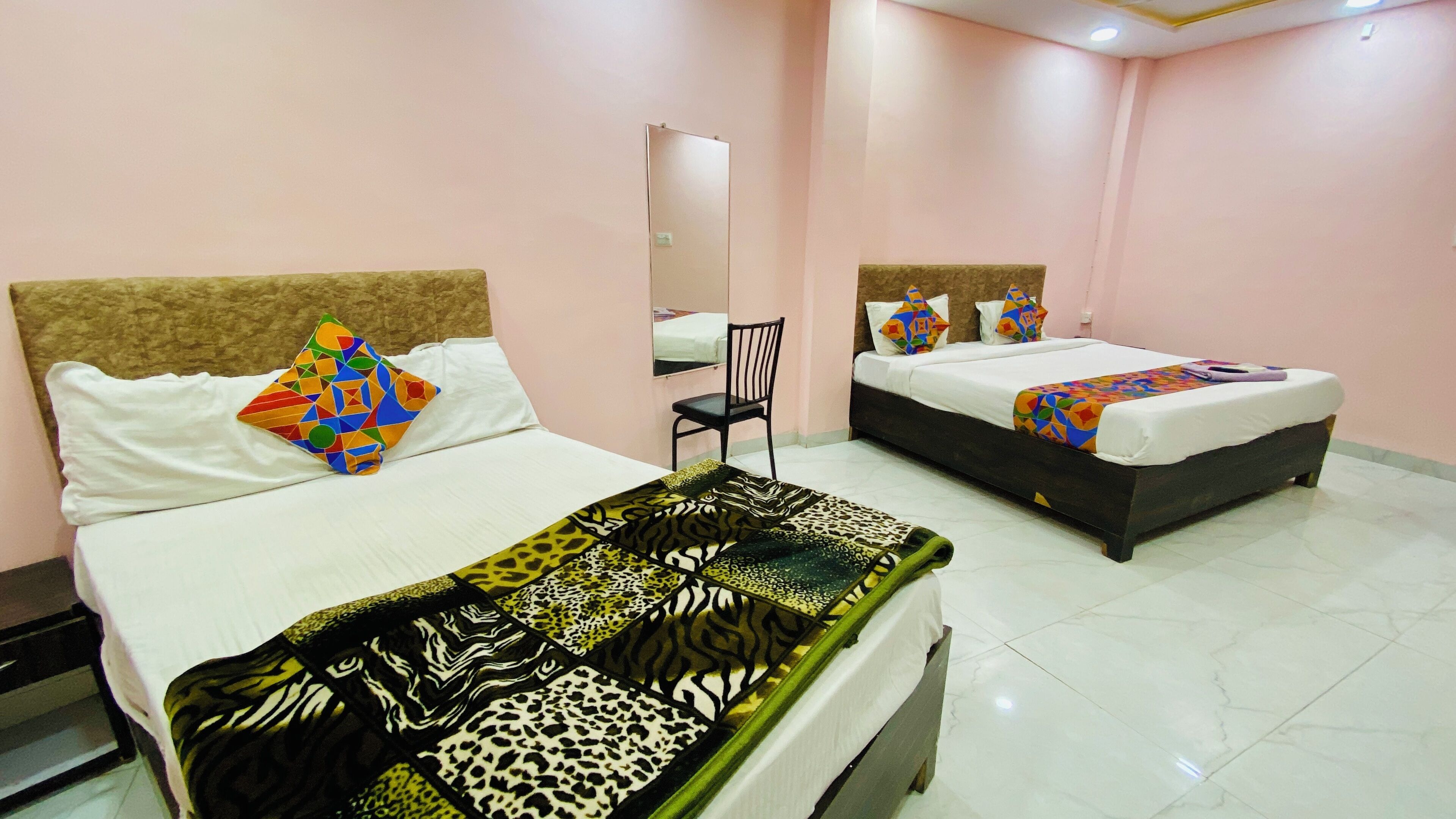 A hotel room with two beds, each with a headboard, a chair, and a mirror on the wall.