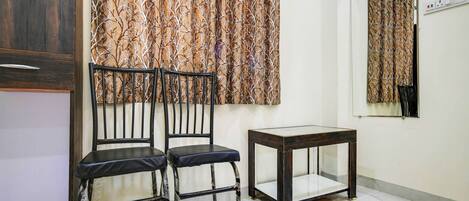 A room with two black chairs, a small wooden table, and a window with patterned curtains.