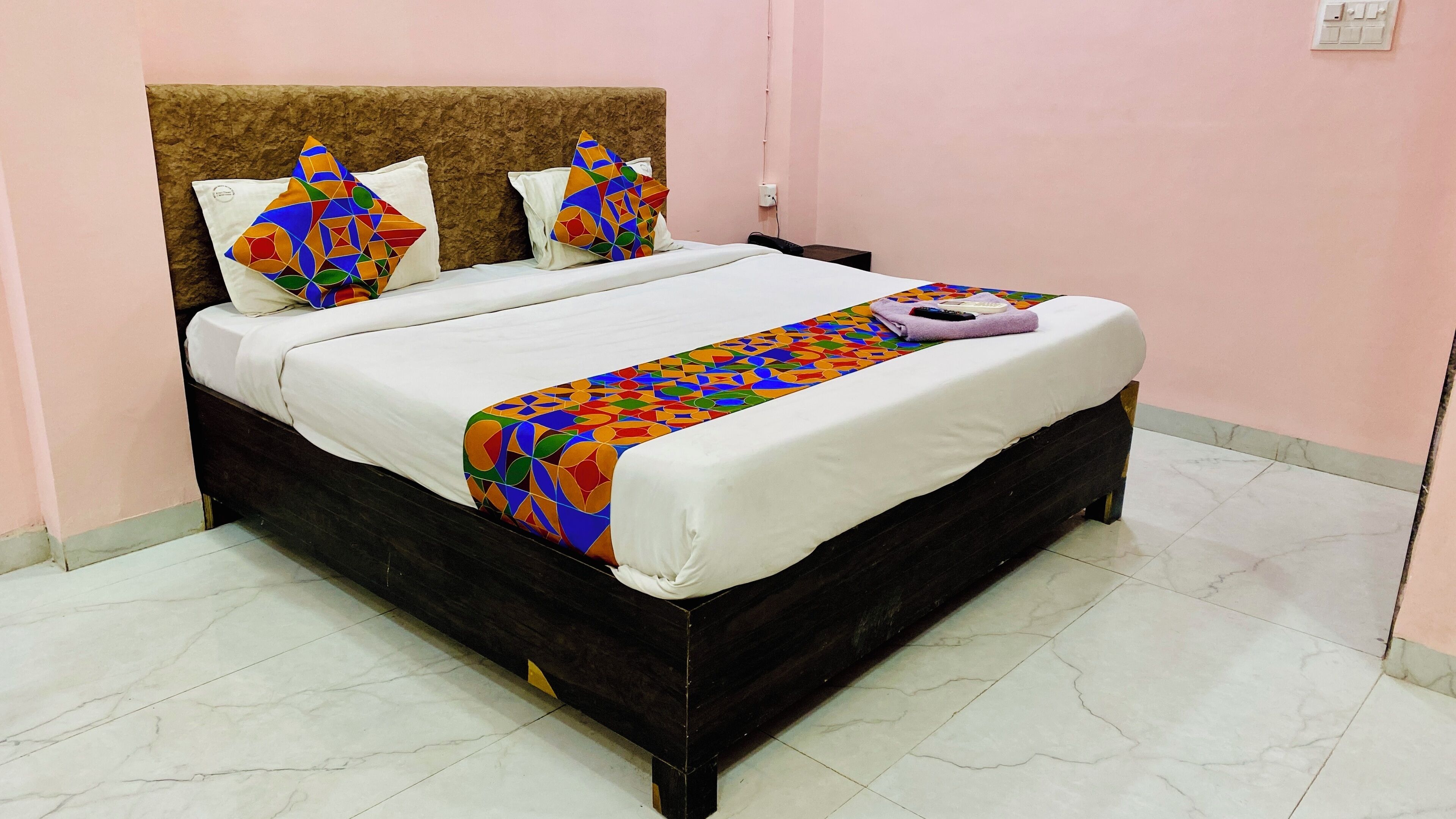Una cama con colcha estampada y almohadas, un cabecero y una mesita de noche con un control remoto y un teléfono.