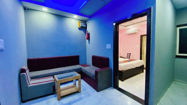 A small, modern room with a sofa, a small table, and a bed. There is a door leading to another room. - Hotel Dev Shree (Indore)