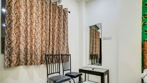 A room with a chair, a small table, a mirror, and a curtain with a leaf pattern. - Hotel Dev Shree (Indore)
