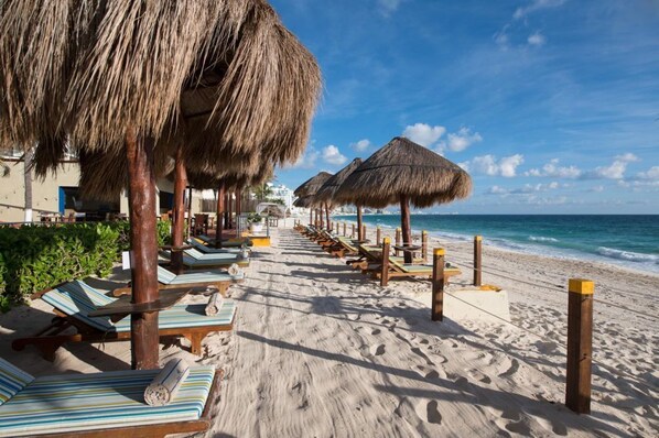 Une plage avec des parasols en chaume, des chaises longues et une vue dégagée sur l’océan.
