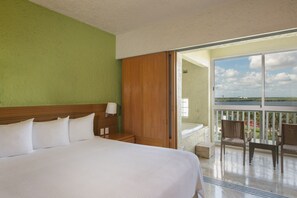 Camera d'albergo con un letto grande, una testiera in legno, un comodino, una lampada e vista su un balcone con sedie.