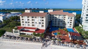 Un hotel con varias plantas, piscina y zona de playa con sombrillas.