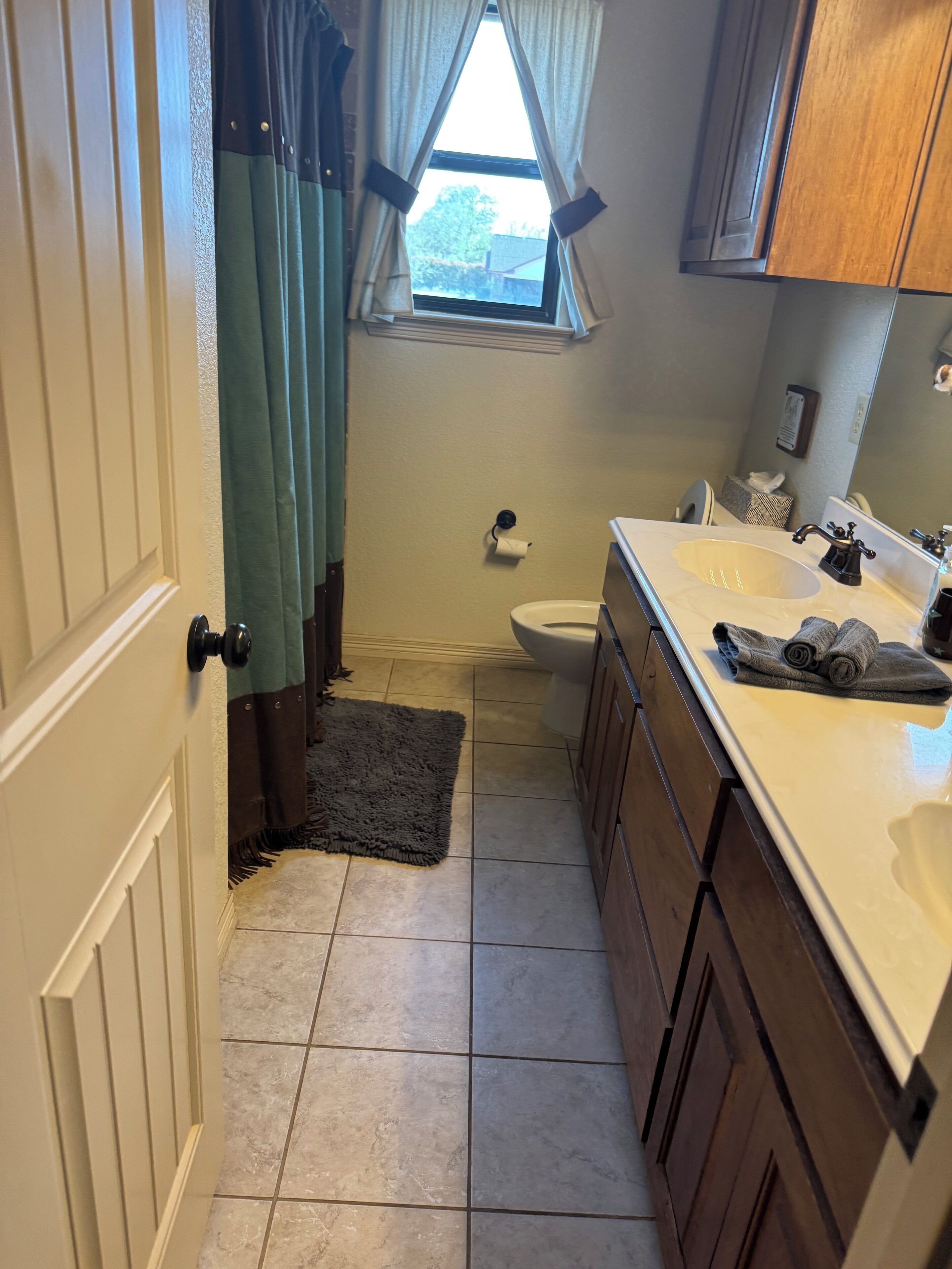 A narrow bathroom with a toilet, sink, and a window with curtains.