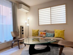A modern living room with a glass-top coffee table, a sofa with patterned cushions, a chair, and a floor lamp.