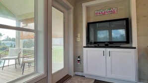 Ein Wohnzimmer mit einem großen Fenster, einem flachbildfernseher an einer weißen Kommode und einem kleinen Teppich auf dem Holzboden.