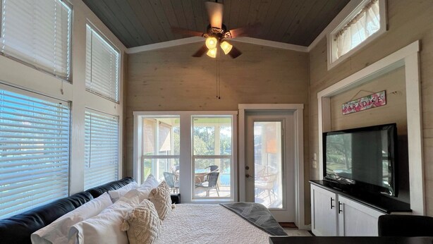 Ein Schlafzimmer mit Bett, Deckenventilator, Fernseher und Blick ins Freie.