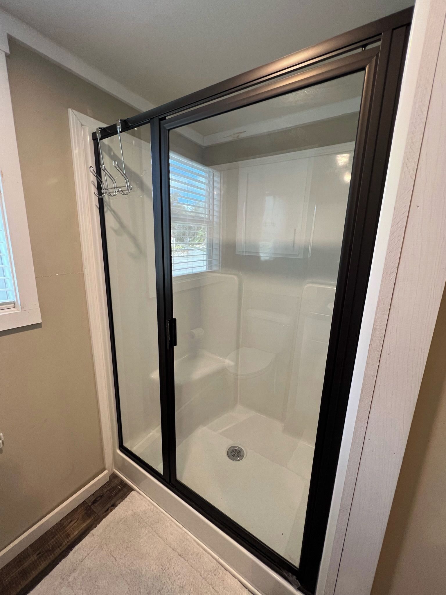 Un espace douche fermé par des parois de verre, avec des toilettes blanches et une petite fenêtre.
