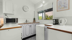 A modern kitchen with white cabinetry, a microwave, a coffee maker, and a window with a view of greenery. - Surfrider Studio - Pet Friendly - 50m to Beach - Book 3 Nights, Pay for 2 until 24 September 2026 (Culburra Beach)