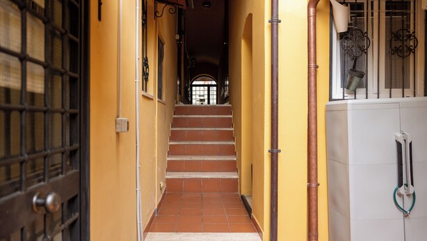 Un corridoio stretto con una scala piastrellata che conduce a una porta con un cancello in metallo.