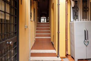 A corridor with a tiled floor, a staircase, a door with a metal grille, and a white cabinet with a hose. - Studio House da Pasolini a Mastroianni (Rome)