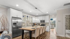 A modern kitchen with white cabinets, stainless steel appliances, and a wooden dining table.