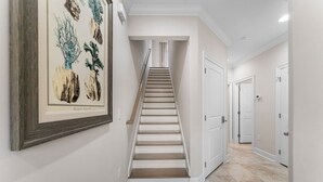 A hallway with a staircase leading to a landing, white walls, and a framed botanical illustration.