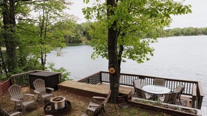 Eine Terrasse mit Gartenmöbeln, einem Feuerkorb und Blick auf einen See.