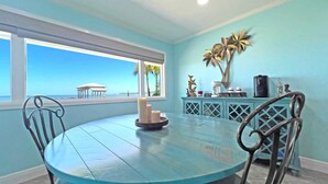 A dining area with a round table, two chairs, a window with a view of the ocean, and a decorative cabinet with a coffee maker. - Hidden Gem, New Patio, Private Dock (Santa Rosa Beach)