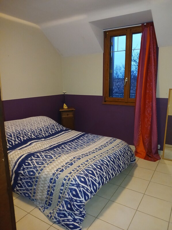 A bedroom with a bed, a nightstand, a window with curtains, and a view of the outside. - Cozy Country Apartment (Terranjou)