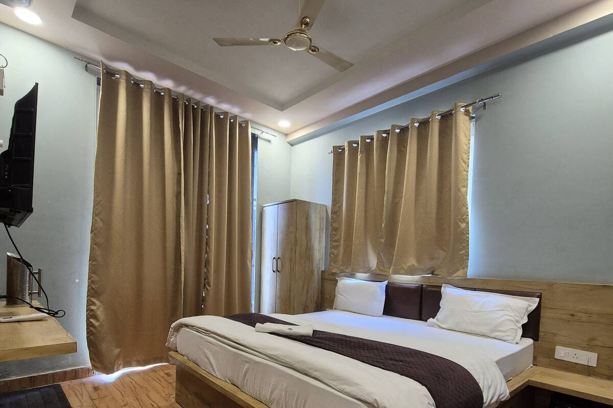 A bedroom with a wooden bed, beige curtains, a ceiling fan, and a television on a stand.