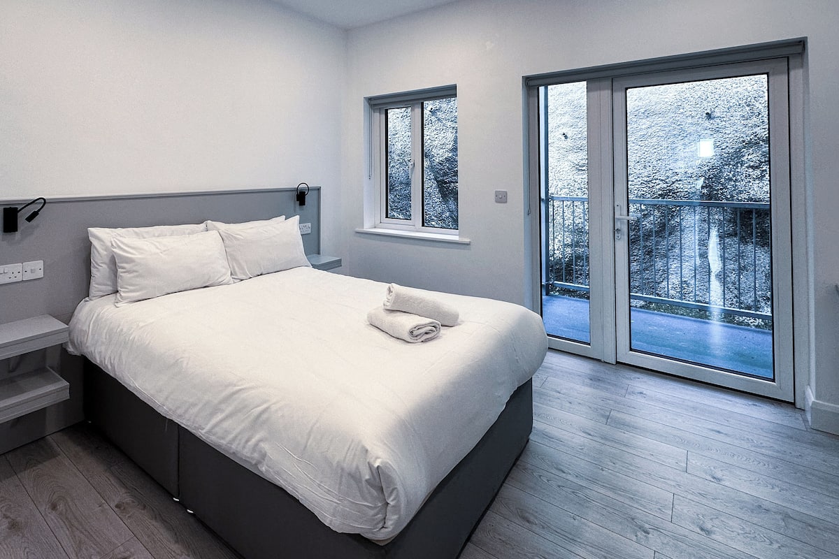 Een moderne slaapkamer met een bed, nachtkastjes, een raam en uitzicht op de omgeving.