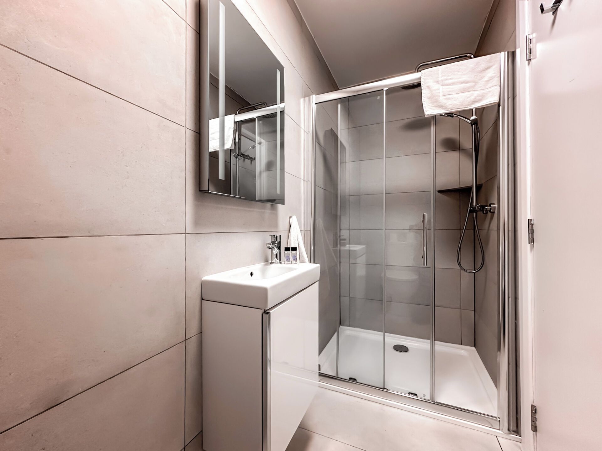 Een moderne badkamer met een douchecabine van glas, een witte wastafel en een grote spiegel.