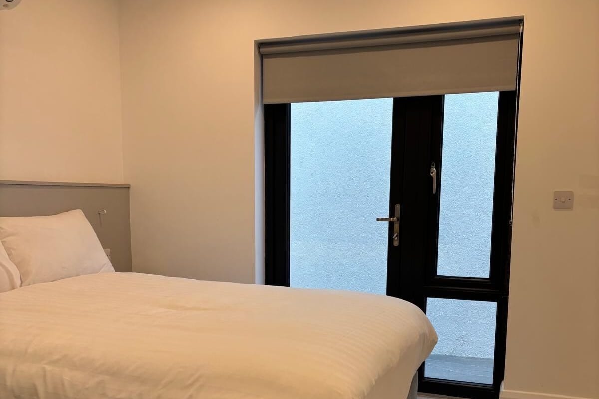 Een slaapkamer met een bed, een raam en een deur naar buiten.