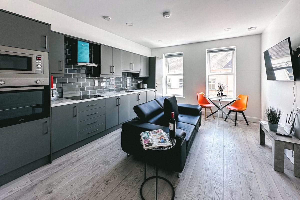 Een moderne keuken met inbouwapparatuur, een eethoek met tafel en stoelen, en een bank.