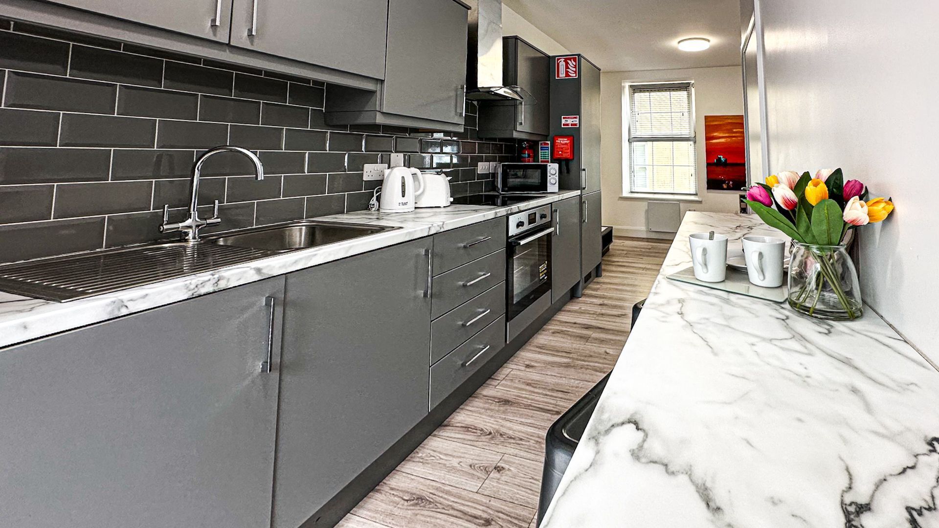 A modern kitchen with grey cabinets, a stainless steel sink, and a marble countertop.