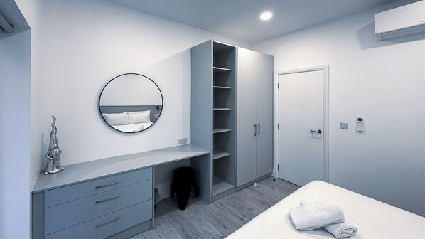 A modern bedroom with a built-in wardrobe, a round mirror, a bedside table, and a neatly made bed. - Cobh Cork Urban Retreats (Cobh)