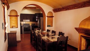 Un comedor con una mesa larga dispuesta para una comida, una cocina contigua con electrodomésticos modernos y una zona de estar acogedora con chimenea.