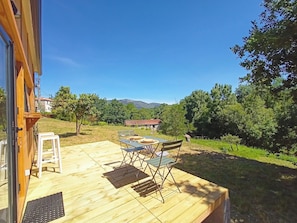 A wooden deck with a table and chairs, overlooking a grassy area with trees and a distant building. - Sistelo - Sleeps4 - Naturalpool- Garden - Parking (Arcos de Valdevez)