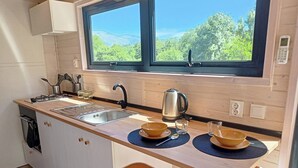 A compact kitchen with a sink, stove, and kettle, two stools, and a window with a view of greenery. - Sistelo - Sleeps4 - Naturalpool- Garden - Parking (Arcos de Valdevez)