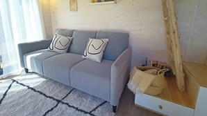 A cozy room with a grey sofa, two pillows, a white rug, and a wooden shelf with pictures and a basket. - Sistelo - Sleeps4 - Naturalpool- Garden - Parking (Arcos de Valdevez)