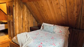 Een gezellig slaapkamer op zolder met een schuin houten plafond, een bed met bloemenbedrukking en een klein nachtkastje.